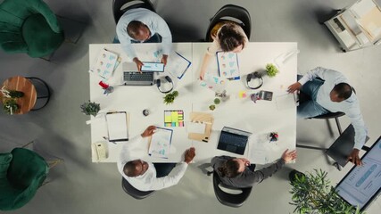 Top down view zoom in of colleagues checking archived files in workplace, reviewing charts and analytics. Employees discuss project progress, report writing and data visualization. Camera A.