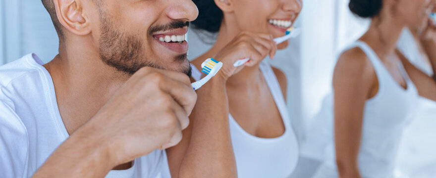 Two adults are smiling while brushing their teeth in a bright and modern bathroom. They are engaged in a healthy morning routine, promoting dental hygiene together. - Powered by Adobe