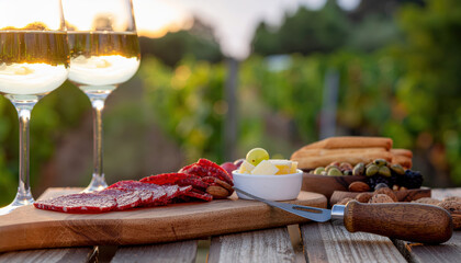 Sunset vineyard picnic with wine glasses, charcuterie slices, cheese cubes, olives and breadsticks creating warm relaxed atmosphere
