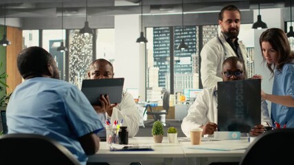 Physicians and medics gathered for briefing conference in boardroom. Group discusses healthcare advancements, laboratory research and treatment methods to enhance medical care. Camera B.