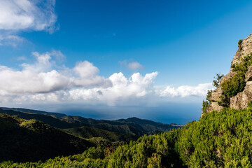 Scenic mountain landscape with lush greenery and dramatic clouds under a bright blue sky, showcasing the beauty of nature and the tranquility of outdoor exploration
