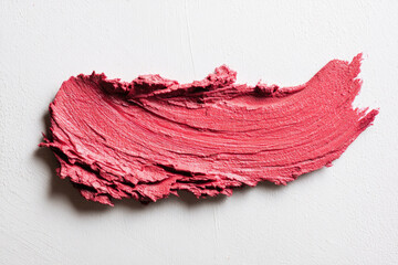 Lipstick smudge swatch in vibrant pink shade displayed from top view on white textured background showing creamy texture and bold color