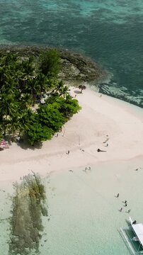 Tiny tropical island with coconut trees, sandy beach and boats anchored on turquoise water. Siargao, Philippines.
