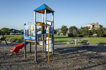 A small neighbourhood playground in Tarneit, Australia, featuring play equipment and nearby picnic tables, within a suburban park, with residential houses in the background. A community outdoor space