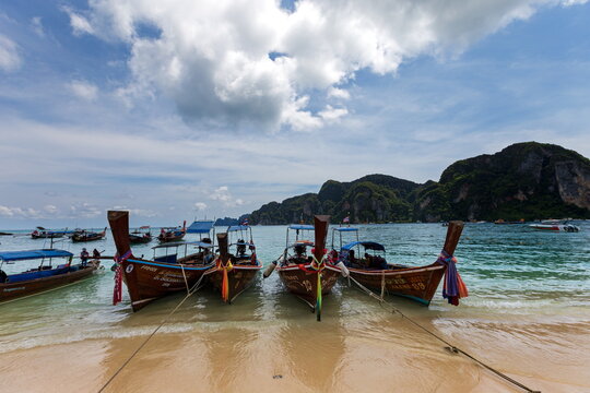 View of traditional longtail boats resting on the sandy beach, the turquoise waters gently lapping against the shore, Phi Phi Island, Krabi, Thailand.