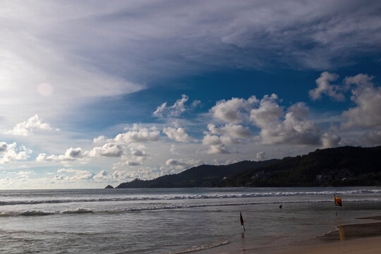 View of the tranquil beach with gentle waves kissing the shore under a sky brushed with clouds, framed by distant lush hills, Phi Phi Island, Krabi, Thailand.