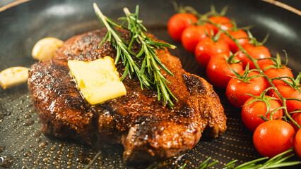 Rare rump steak sizzling in a pan with cherry tomatoes, garlic, and rosemary. Butter melting over the steak, creating a golden crust. Juicy and aromatic cooking process.