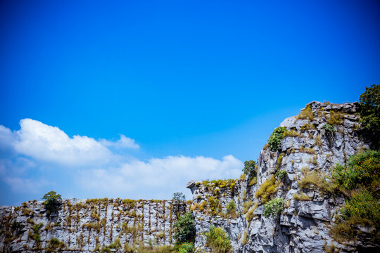 View of a rugged cliff face etched with time stands boldly against the vast expanse of a pure blue sky in Mpape, Abuja, Federal Capital Territory, Nigeria.