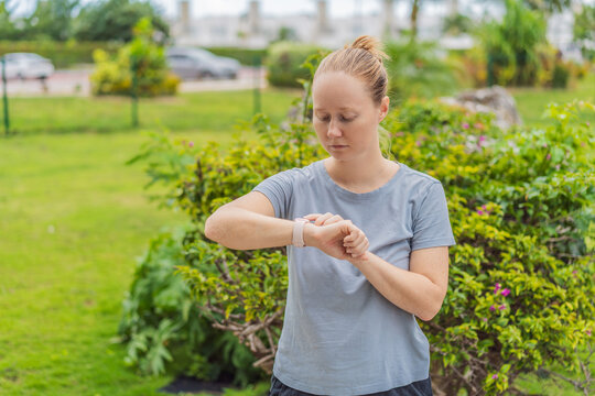 A woman standing in a park and checking her fitness watch before starting her workout. Outdoor exercise, health tracking, wellness routine, motivation and active lifestyle concept - Powered by Adobe