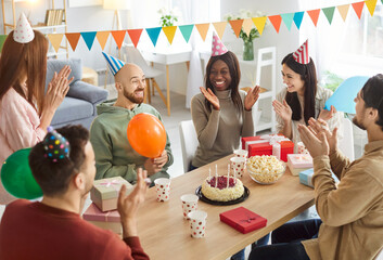 Portrait of happy joyful friends group celebrating Birthday party sitting at festive table in the living room at home. People gathering together congratulating friend on holiday. Celebration concept.