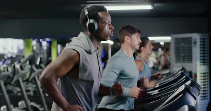 Headphones, training and man on treadmill in gym for running, workout or fitness with health. Wellness, audio tech and male person listening to music for cardio exercise on machine in sports center.