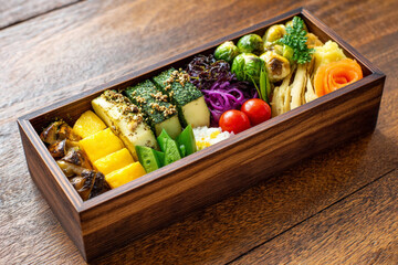 Colorful bento box filled with vegetables, rice, and tropical fruit arranged neatly on a wooden table