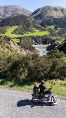 A motorcyclist is relaxing on a gravel road, enjoying the view of a picturesque mountain valley