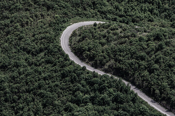 Aerial or aerial view of a sharp mountain bend surrounded by dense green forest cover. The winding...