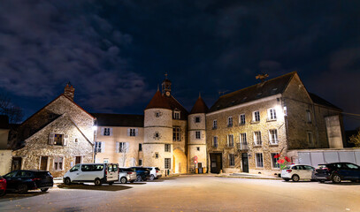 Night view of the historic town hall of Tournan-en-Brie in Paris Region of France. The stone town hall and surrounding buildings are illuminated under a cloudy dark sky
