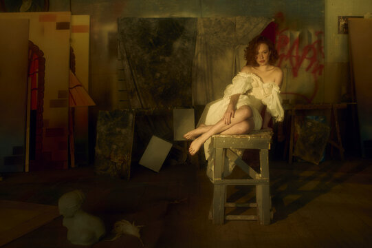 barefoot woman in a vintage dress is sitting on the wooden stool 