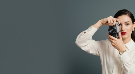 Elegant woman photographer holding a vintage camera. Stylish female artist taking a picture on a grey background with copy space