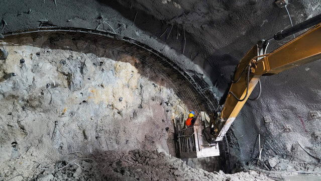 Tunnel Construction: Worker, Excavator Arm, and Shotcrete Application