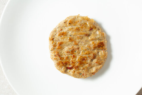 A top down view of a single chicken sausage patty, on a plate.