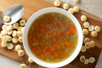 A top down view of brothy soup bowl, featuring a pile of oyster crackers.