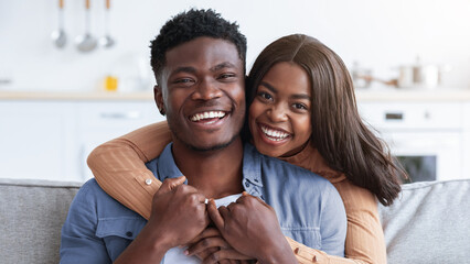 A joyful couple is sharing a happy moment in their cozy living room. They are embracing and smiling widely, radiating love and happiness while seated on a comfortable couch.