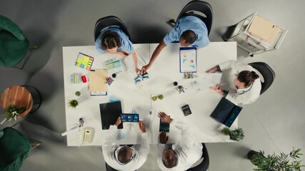 Top down view zoom in of doctors team in a collaborative meeting discussing therapy, diagnostics and clinical coordination. Modern staff focuses on communication and patient health. Camera A. - Powered by Adobe