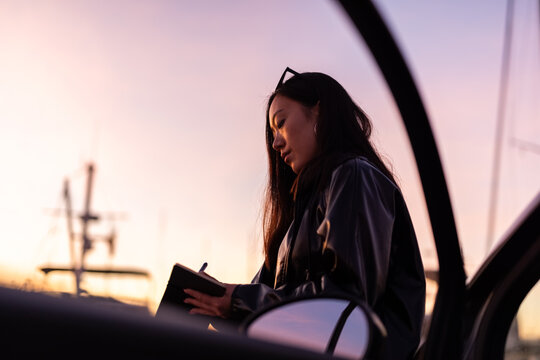 Woman Writing in a Notebook During Sunset Near a Boat Dock