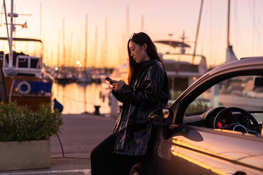 Woman Checking Her Phone by the Harbor at Sunset