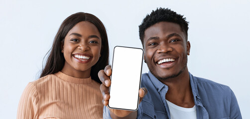 Two friends stand close together, both smiling brightly. One friend holds up a smartphone with a...