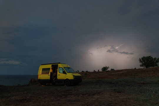 Stormy Night With Yellow Van Parked Near Water Under Lightning