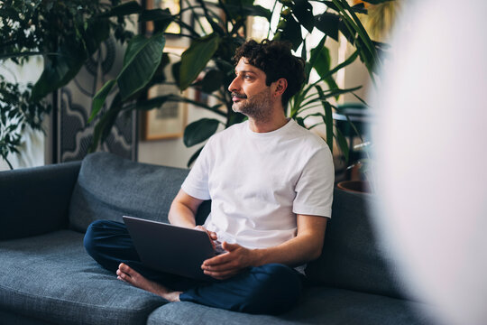 Man Sitting on Couch Using Laptop in a Bright Home Setting