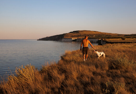 Man Walks With Dog Along Coastal Grassland at Sunset