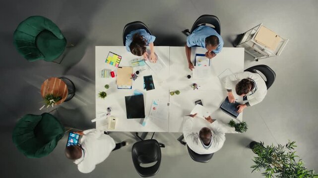 Top down view of diverse physicians team reviewing clinical records, working together and sharing expertise to improve healthcare services at the hospital. Brainstorm treatment ideas. Camera A.