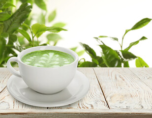 Matcha latte in cup on wooden table against green leaves. Space for text