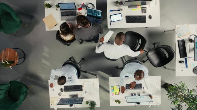 Top down view zoom in of employees collaborating on planning business strategy. Colleagues sharing market data, performance reports and insights, aligning goals and resource allocation. Camera A.