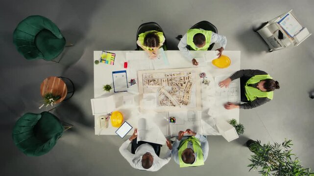 Top down view of developers in modern office environment planning construction. Architects and engineers discuss site preparation, master plan updates and real estate investment. Camera A.
