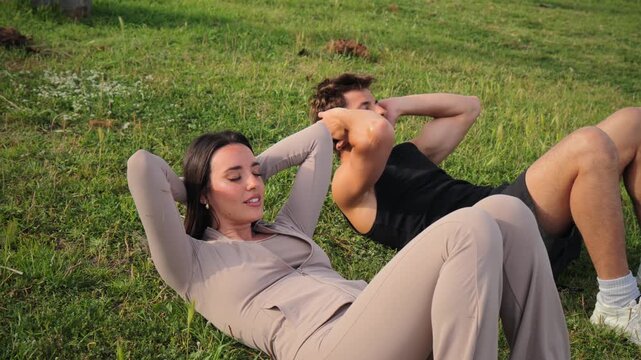 A couple engages in rigorous abdominal workouts on grass, demonstrating dedication to health and fitness through their intense training and commitment to physical well-being and strength building.