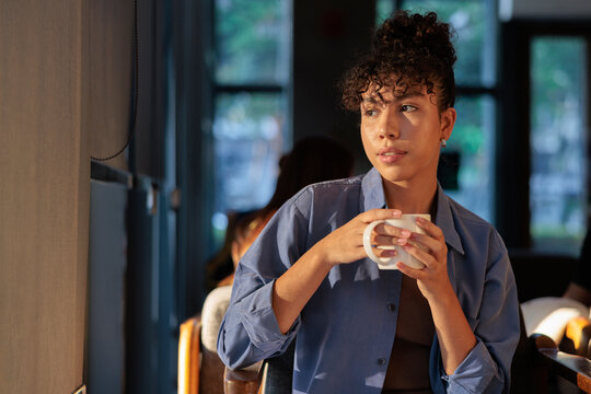 Woman with coffee looks thoughtfully out window.