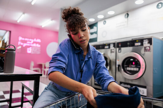 Woman on phone doing laundry at laundromat.
