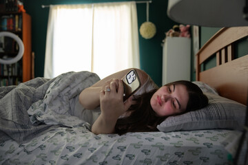 Woman relaxing in bed holding smartphone in comfortably lit room