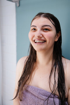 Smiling young woman with wet hair wrapped in a towel after shower