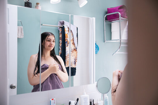 Young woman in bathroom mirror reflection holding a purple towel