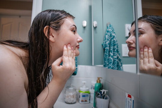 Woman examining her facial skin in the bathroom mirror