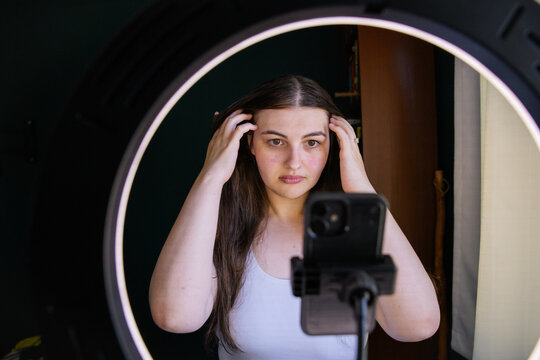 Woman styling her hair near a smartphone and ring light at home