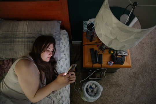 Young woman in bed using a smartphone, surrounded by personal items