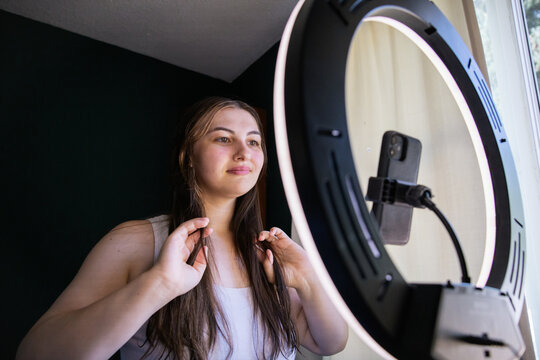 Young woman recording video with smartphone and ring light