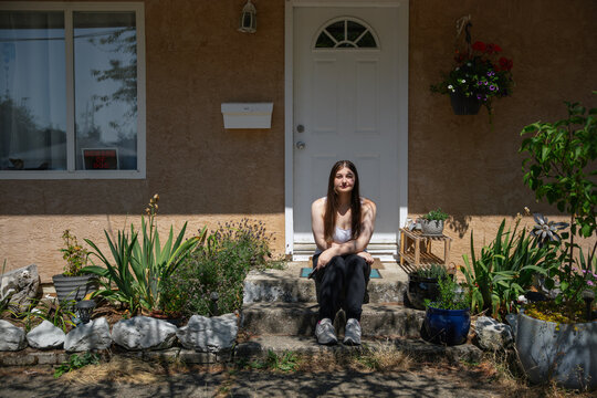 Young woman sits on a garden step in front of her home with cell 