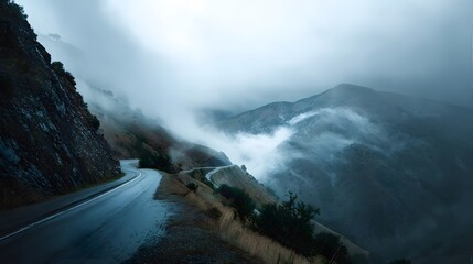 A winding mountain road disappears into thick mist on a rainy, overcast day.