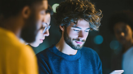 Young creative team brainstorming mobile app design modern night office, focused developer using smartphone, coworker collaboration, startup project planning, cinematic mood, technology teamwork