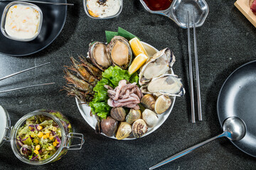 A white plate of assorted raw seafood including oysters, clams, abalone, shrimp, and squid, garnished with lettuce and lemon, with sauces nearby.
